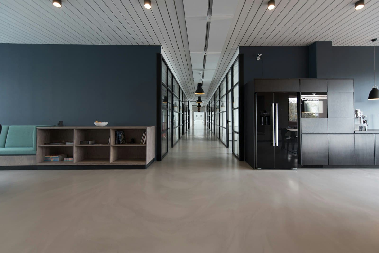 A long studio corridor with glass rooms and a dark wall