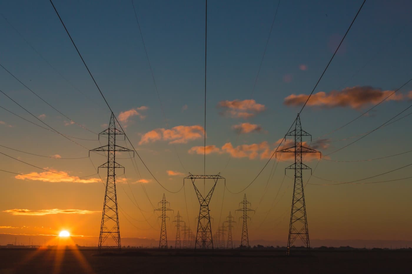 High-voltage pylons receding across a plain at dusk